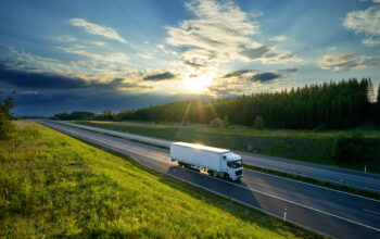 White truck driving on the highway in the countryside in the rays of the sunset with dramatic clouds